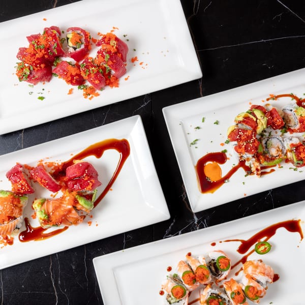 Four white rectangular plates filled with various colorful sushi rolls on a black marble surface.