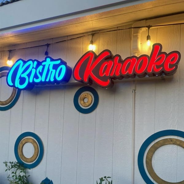 Neon signs for "Bistro" in blue and "Karaoke" in red on a white wooden wall.