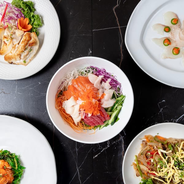A top-down view of various Japanese dishes, including sashimi, noodles, and grilled fish, on a black marble table.