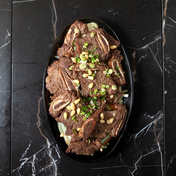 Galbi short ribs, garnished with pine nuts and green onions, served on a black platter.